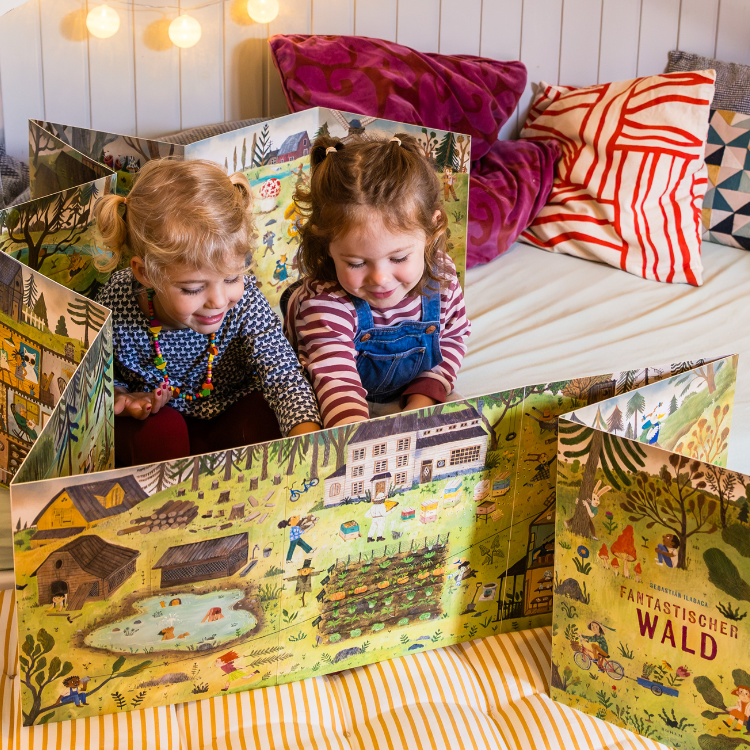 Über uns - Verlag - Bohem Press - fantastischer Wald Foto von zwei Kleinkindern, die sich zusammen ein aufgestelltes Buch "Fantastischer Wald" anschauen
