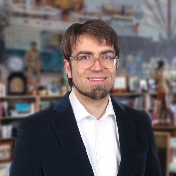 Coppenrath Verlag Geschäftsführer – Dr. Lambert Scheer Mann mit Brille, Hemd und Sakko vor Regal mit Büchern und Geschenkartikeln