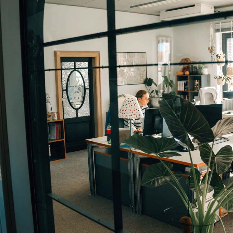 Anzeigebild Kontakt Vertrieb Glasfront vor Büro, unscharf Frau am Schreibtisch zu sehen