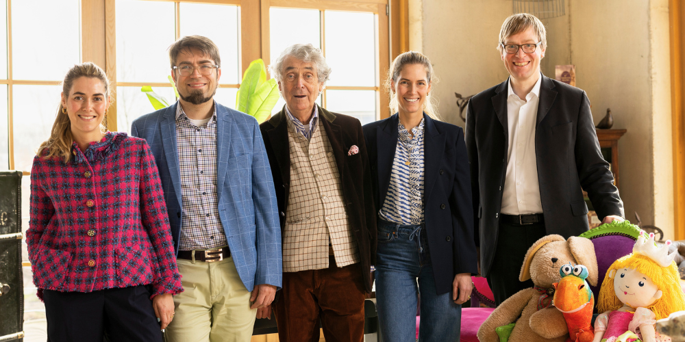 Coppenrath „Über uns“ – Geschäftsleitung März 2025 Das Bild zeigt die fünf Mitglieder der Geschäftsleitung: Wolfgang Hölker, Dr. Lambert Scheer, Johanna Hölker, Louisa Hölker und Dr. Burkhard Scheer stehend vor Fenster in Büro mit Pflanzen und Teddy