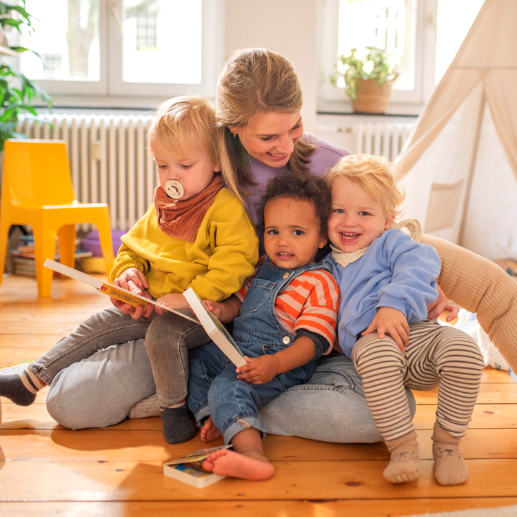 Frau sitzt mit drei kleinen, lachenden Kinder und Büchern in einem gemütlichen kinderzimmer.